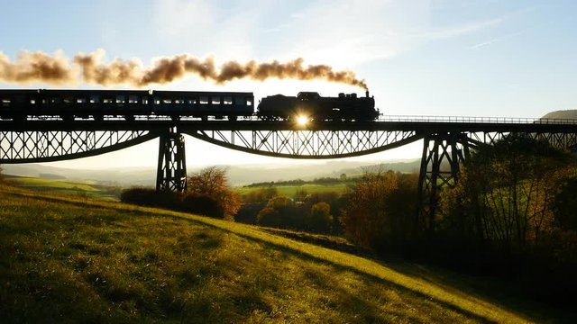 silhouette of locomotive train crossing bridge road at sunset magic hour.