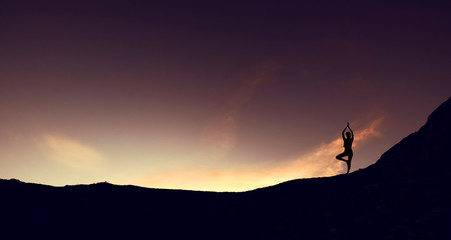 Silhouette mountain edge young woman practicing yoga on mountain in sunrise