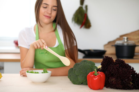 Young woman is cooking healthy meal from vegetables at the kitchen. Close up of housewife with wooden spoon pointing into salad and brocolli. Vegetarian concept.