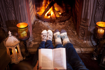 Couple relaxing at home reading a book. Feet in wool socks near fireplace. Winter holiday concept