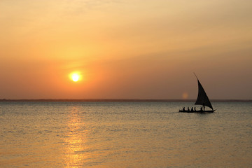 Sunset over the ocean with a sail boat heading toward the right side
