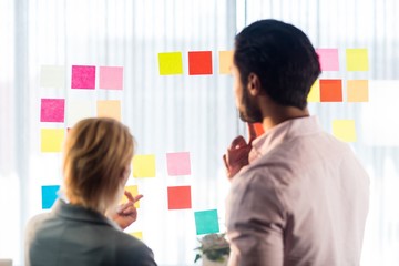 Rear view of two business people looking at post it wall 