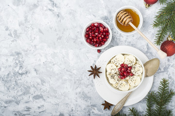 Healthy breakfast oatmeal with pomegranate, bananas, seeds and nuts, overhead scene on white marble. Top view