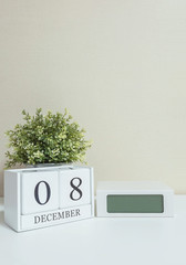 White wooden calendar with black 8 december word with clock and plant on white wood desk and cream wallpaper textured background , selective focus at the calendar