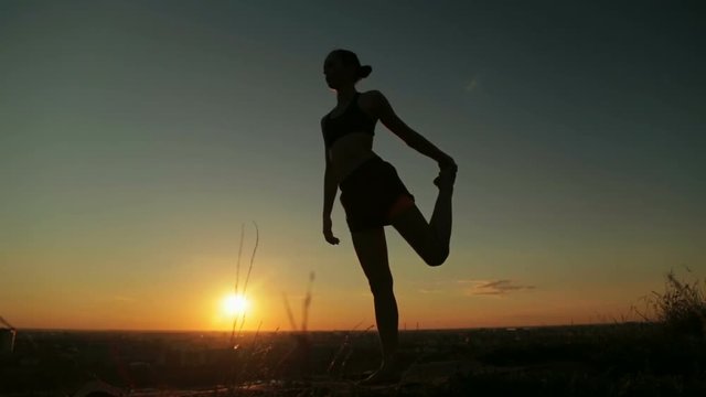 Silhouette of sporty woman practicing yoga in the park at sunset - lord of the dance pose. Sunset light, golden hour. Freedom, health and yoga concept