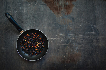 The failure on kitchen: burnt charred vegetables in frying pan on dark shabby background