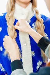 Stylist's hands braids pigtail for Snow Maiden. Cropping. Girl with blond hair in a blue Christmas suit.