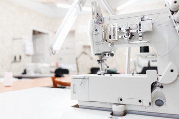Professional garment factory office, free space. Sewing machine on foreground, blurred workroom for seamstresses on background. Clothes making industry concept