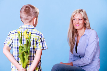 Little boy with mother hold flowers behind back.