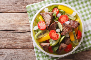 Delicious Salad with beef, kiwi, tomatoes, pepper and herbs close-up. horizontal top view