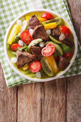 Festive food: Salad with beef, kiwi, tomatoes, pepper and herbs close-up. vertical top view