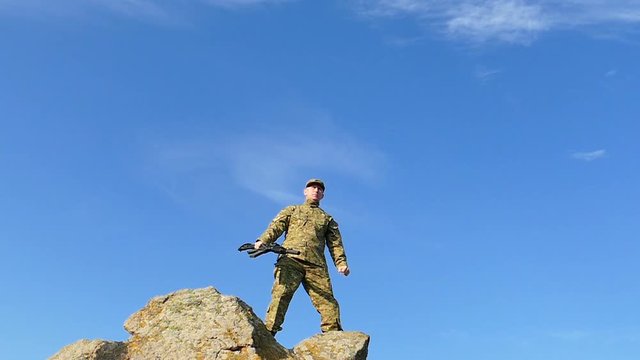 Soldier  lift up hand and   automatic rifle  against blue sky. Slow Motion

