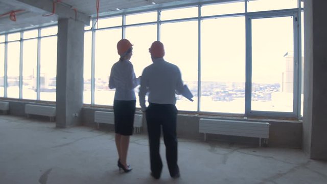 Businessman and business woman in suit, hard hat communicate, discuss blueprint, construction site. 4K.