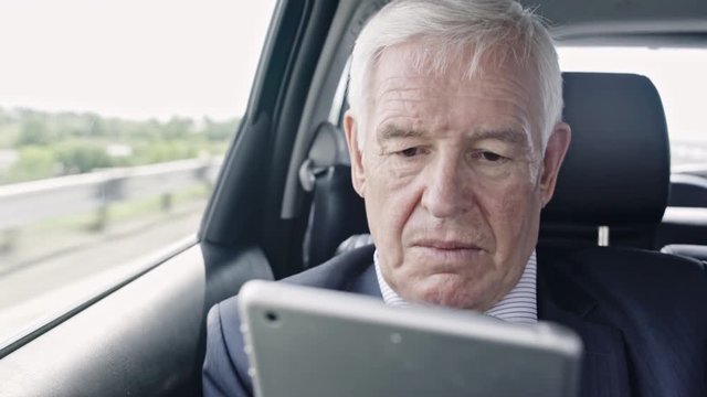 Busy senior businessman sitting in car on bumpy road and working on his tablet
