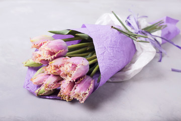 Bouquet of lilac tulips wrapped in lilac paper. Still life with colorful tulips. Fresh spring tulips.  Place for text. Flower concept. Fresh spring bouquet. Summer Background