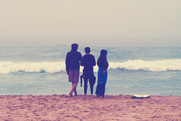 Three surfers stand ashore ocean. Instagram.