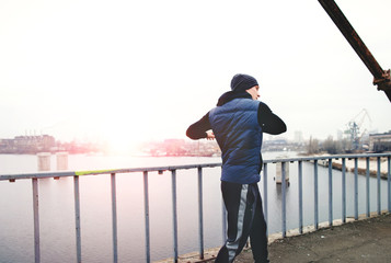 Athletic young man in sports clothing training on city bridge