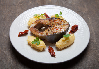 Fried tuna fish with mashed potato, dried tomato and parsley on