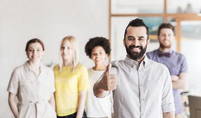 happy man showing thumbs up over team in office