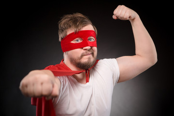 Portrait of funny super hero mn with red msk on showing his strength or force isolated on black...