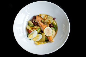 salad with grilled salmon, potatoes chips, boiled eggs and vegetables in white plate and black background