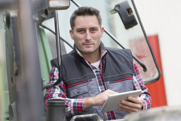 Farmer leaning on the tractor using a digital tablet