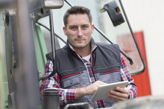 Farmer Leaning On The Tractor Using A Digital Tablet