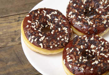 A plate of iced chocolate sprinkle ring donuts on a rustic wooden table background