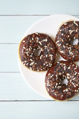 Overhead view of a plate of iced chocolate sprinkle ring donuts on a blue wooden table background