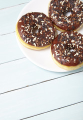 A plate of iced chocolate sprinkle ring donuts on a blue wooden table background with blank space below