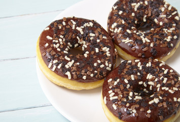 A plate full of iced chocolate sprinkle ring dounuts on a painted wooden background