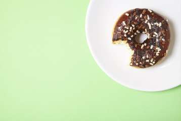 An iced chocolate sprinkle ring donut with bite mark, on a pastel green background with empty space at side
