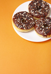 A plate full of iced chocolate sprinkle ring donuts on a bright orange background with blank space below