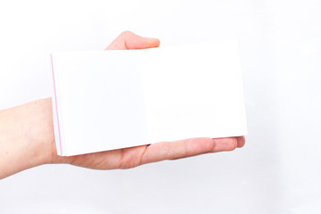 Obraz premium Hand holds notebook open. Blank white paper. Place for an inscription