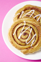 A close up of a plate of freshly baked cinnamon swirls on a bright pink background