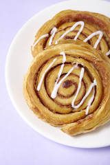 A close up of a plate of freshly baked cinnamon swirls on a pastel purple background