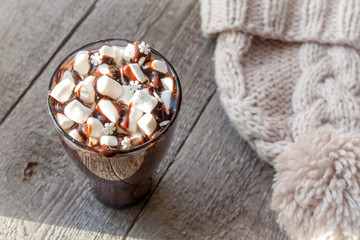 Winter hot cocoa with marshmallows, chocolate syrup, sugar snowflakes in a tall glass on a wooden background.