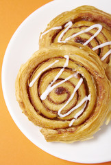 A close up of a plate of freshly baked cinnamon swirls on a bright orange background