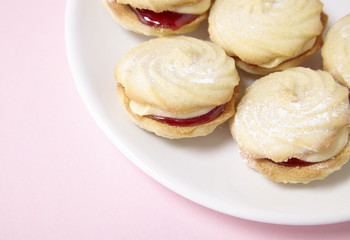 A plate full of freshly baked Viennese whirl biscuits on a pastel pink background