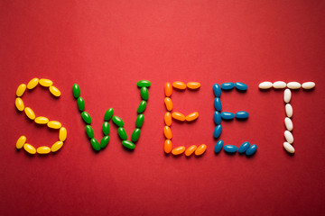 Word sweet from colorful candies on red paper background. 