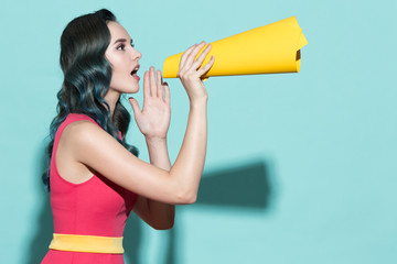 Young beautiful girl speaks in a yellow paper loudspeaker.