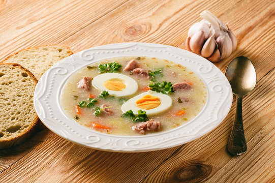 Traditional polish white borscht - zurek, sour soup with white sausages and eggs.
