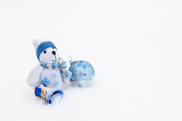Teddy bear sitting on snow with a bell and ball.