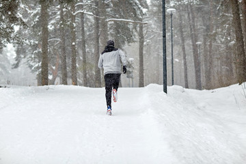 man running on snow covered winter road in forest