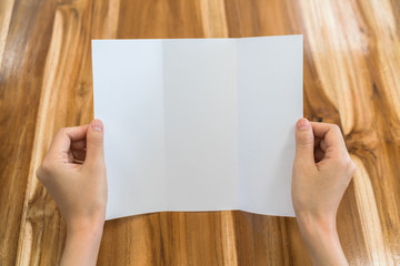 Obraz premium Women hand hold Trifold white template paper on wood texture .