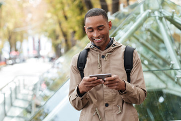 Cheerful young african man playing at phone outdoors