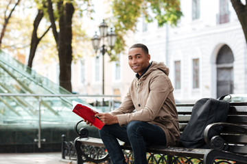 African cheerful man looking at camera while reading a book