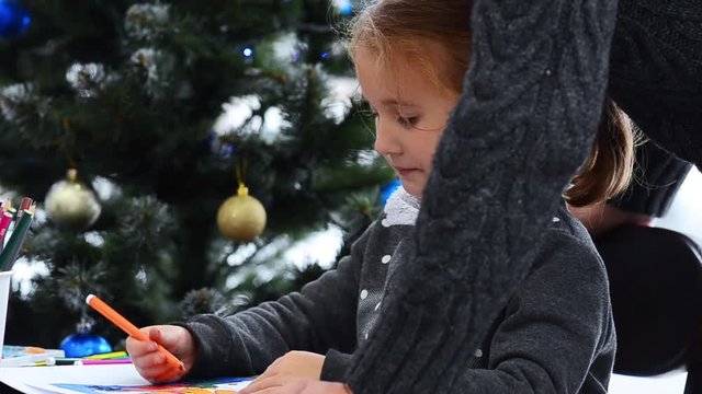 Father helping her daughter in drawing. Watching little girl drawing on paper. Christmas lights background