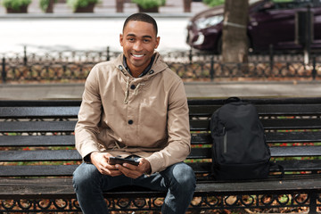 Happy man holding tablet while sitting on wooden bench