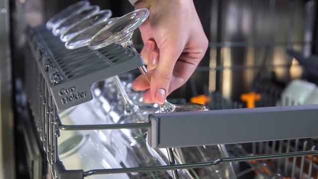 A young woman is putting glasses inside a dishwasher in a nice order. Then she is pushing the shelf inside.
